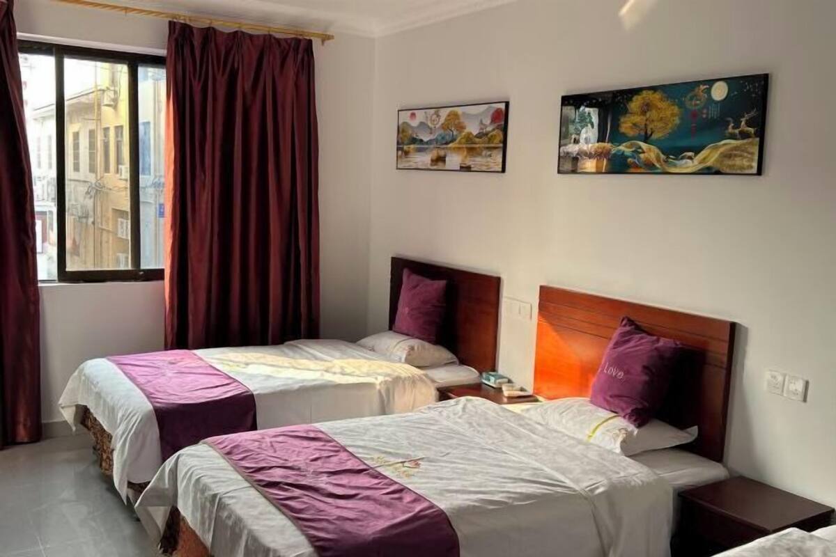 A hotel room with two beds, a window with curtains, and two paintings on the wall.