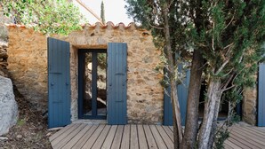 A stone building with a wooden deck, a tree, and a door with blue shutters.