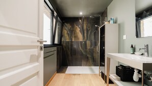 A modern bathroom with a glass shower enclosure, a white vanity with a mirror, and a wooden floor.