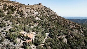 A hillside property with a house featuring a red-tiled roof, surrounded by sparse vegetation and rocky terrain.