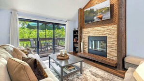 A living room with a fireplace, a sofa, a coffee table, and a TV mounted on the wall. - Ozark Escape - Enjoy Resort-style Fun (Osage Beach)