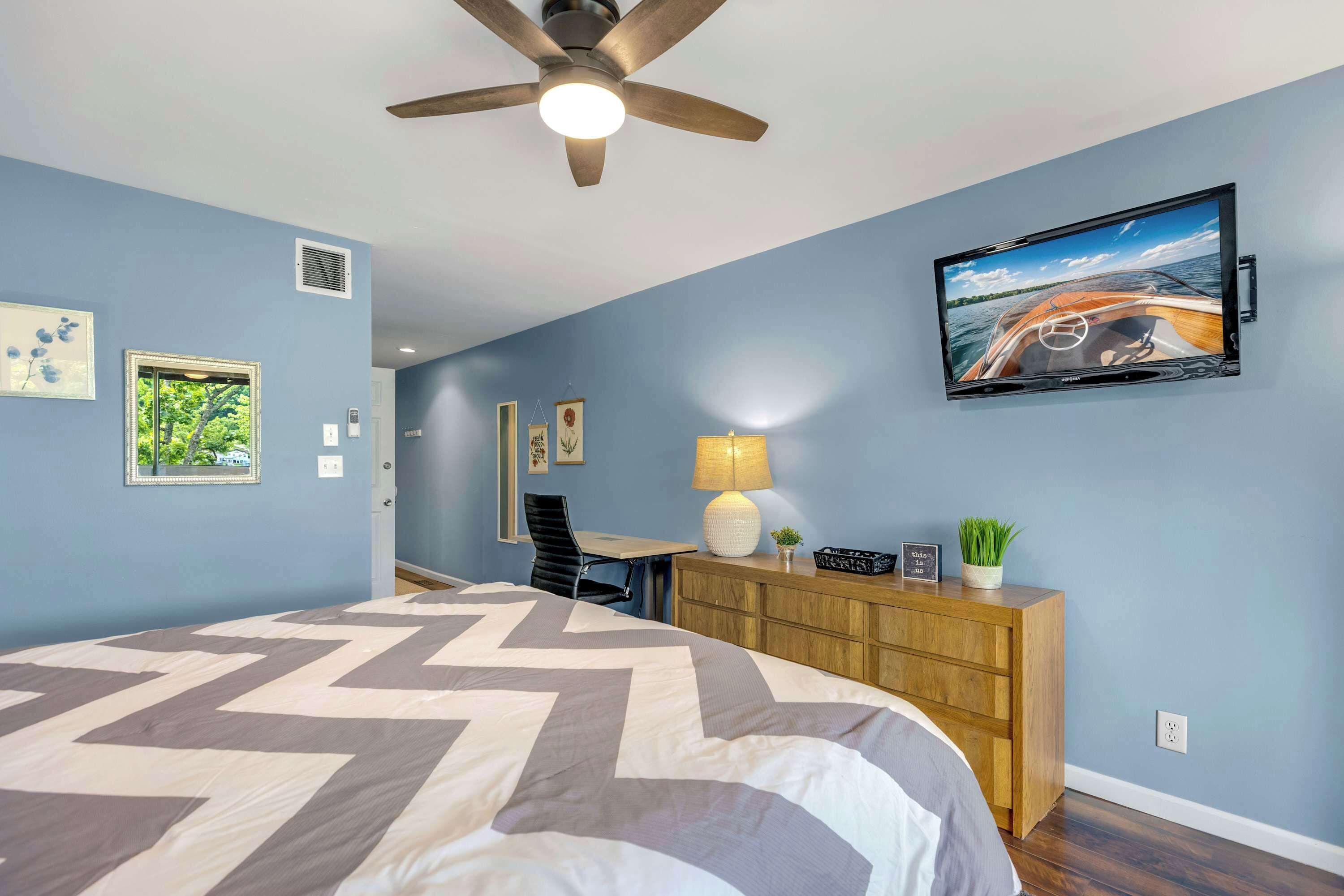 Une chambre à coucher comprenant un lit, un bureau, une chaise, un téléviseur et un ventilateur de plafond.