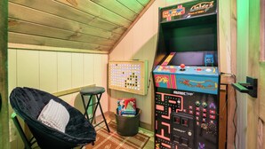A cozy room with a wooden ceiling, a black chair with a white cushion, a small table, and an arcade machine labeled 'Arcade'. - *Modern 3BD Cabin w/ Hot Tub + Arcade! Near TOWN!* (Pigeon Forge)