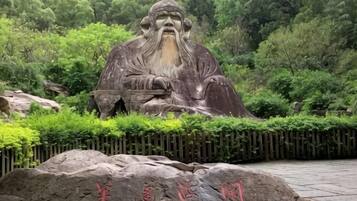 Una gran estatua al aire libre de una figura histórica en un entorno natural, con base de piedra y caracteres chinos.