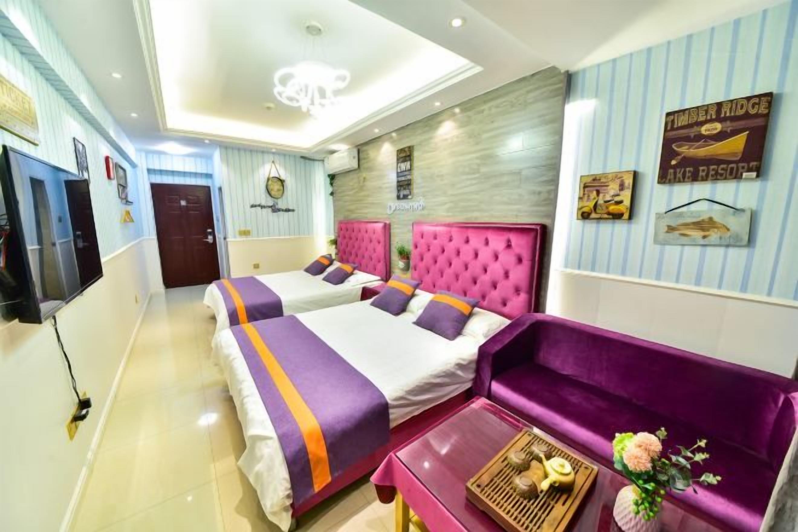 A hotel room with two beds, a sofa, a TV, and a ceiling light.