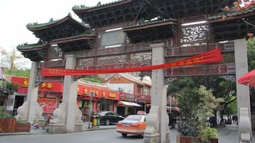A traditional gate with intricate carvings and a red banner, leading to a street with shops and a parked car.