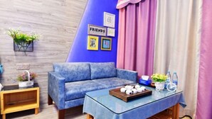 A cozy room with a blue sofa, a glass coffee table with a tray of white balls, a small wooden side table, and a wall with framed pictures and the word "FRIENDS". - Huangsheng Hotel (Quanzhou Food Street) (Quanzhou)