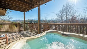 A hot tub under a wooden pergola with a view of mountains and trees.