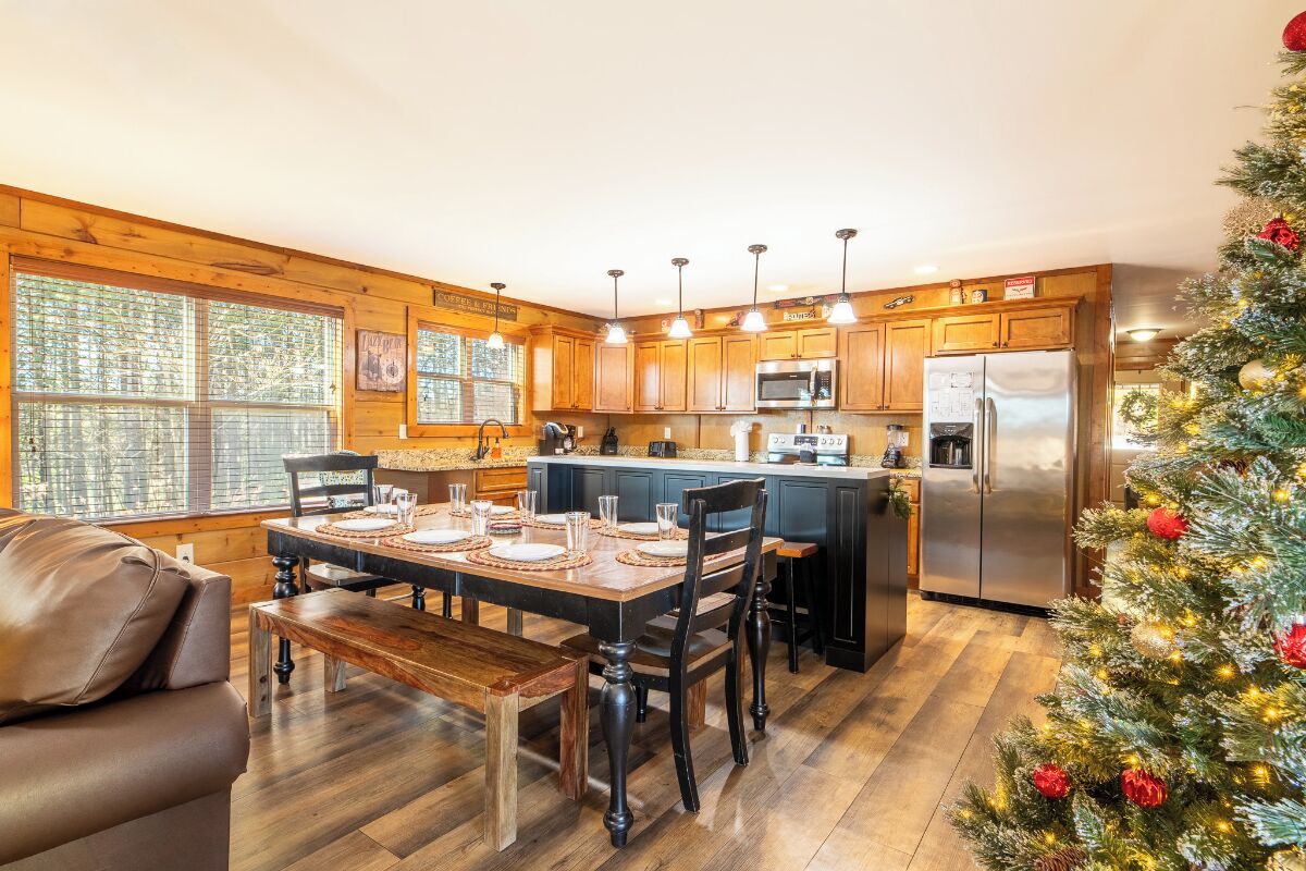 A modern kitchen with wooden cabinets, a central island, stainless steel appliances, and a dining area with a wooden table and benches.