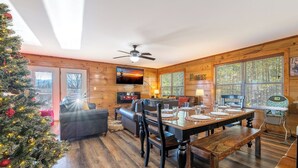 A cozy cabin interior with a dining table set for four, a fireplace, and a Christmas tree.