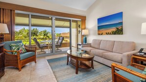A spacious living area with a large sliding glass door leading to a balcony, a beige sofa, a wooden coffee table, and wicker chairs.
