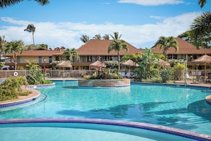 Une piscine de villégiature aménagée dans un cadre tropical, avec des palmiers et des parasols en feuilles de palmier.