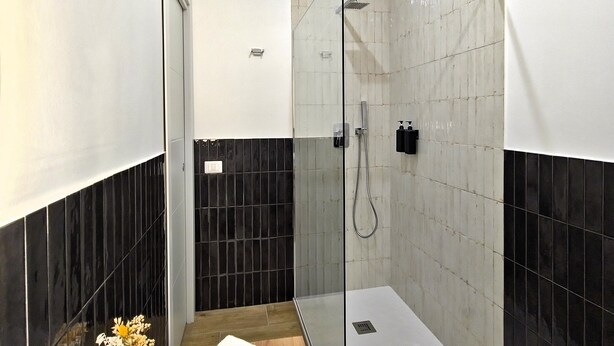 A modern bathroom with a glass shower enclosure, a wooden vanity with towels, and a white bathtub. - Ventuno Dei Luxury Suites - San Giovanni (Rome)