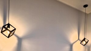 A bed with a yellow headboard and white bedding, a bedside table with a lamp, and a wall with geometric light fixtures.
