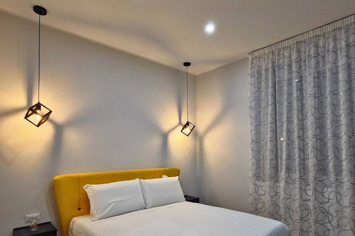 Ein modernes Schlafzimmer mit einem gelben Bett, weißer Bettwäsche und zwei Pendelleuchten.