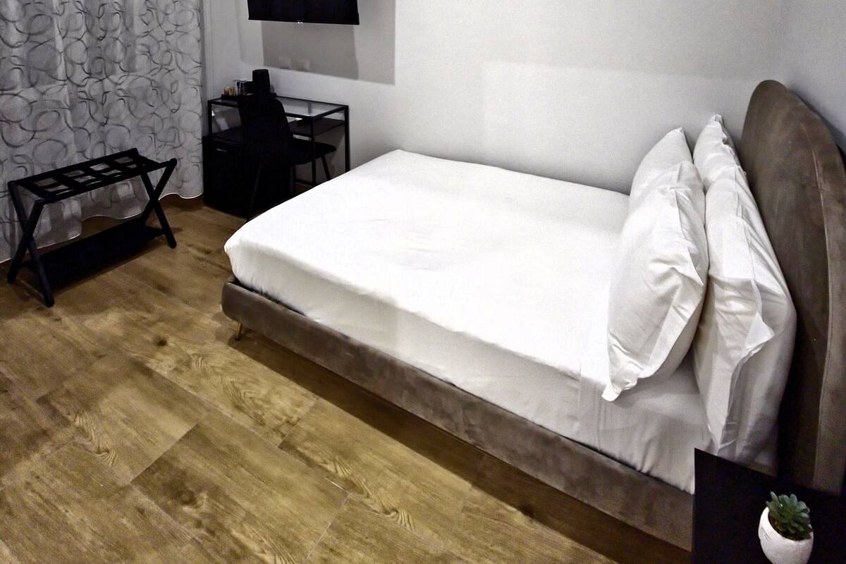 Ein Schlafzimmer mit einem Bett, einem Schreibtisch, einem Stuhl, einem Fernseher und einer kleinen Pflanze.
