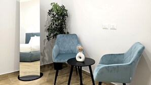 A modern room with a large mirror, two blue armchairs, a small round table, and a potted plant. - Ventuno Dei Luxury Suites - San Giovanni (Rome)