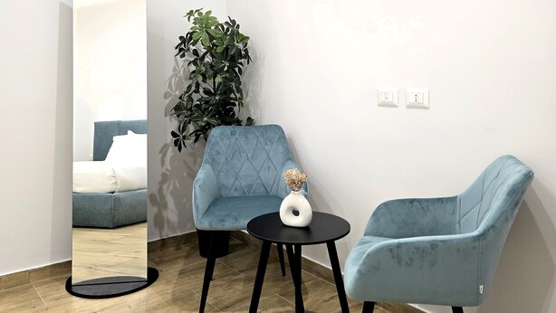 A modern room with a large mirror, two blue armchairs, a small round table, and a potted plant.