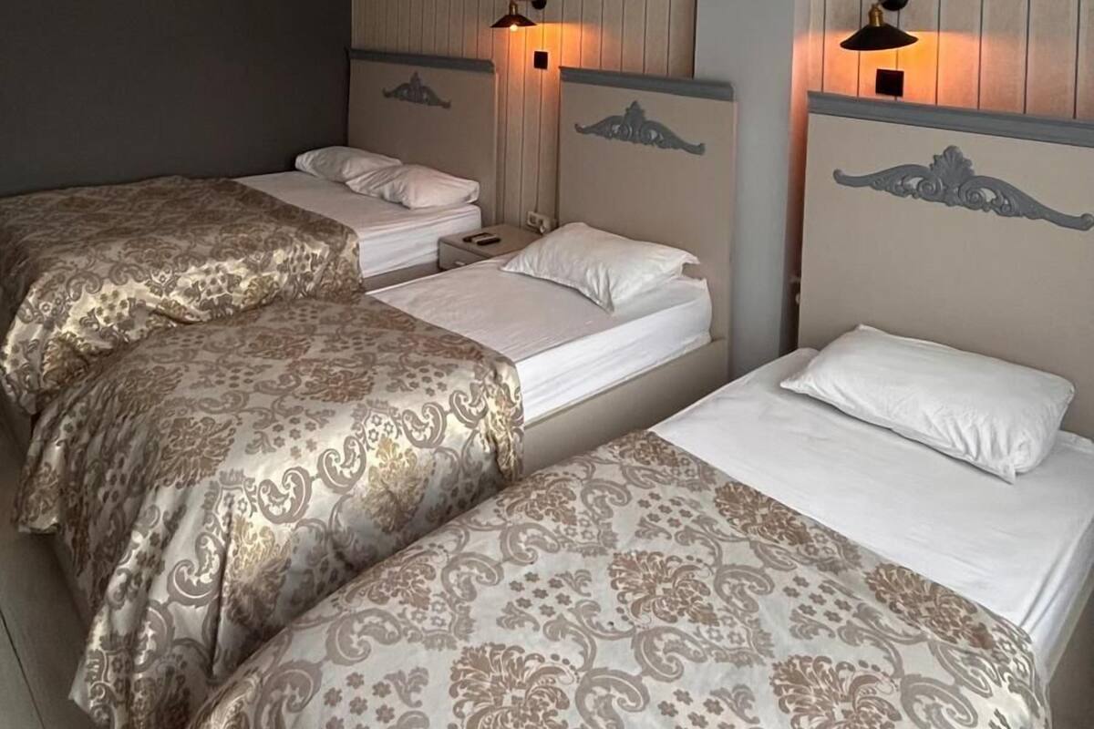 A hotel room with two beds, a ceiling fan, an air conditioning unit, and wall-mounted lamps.