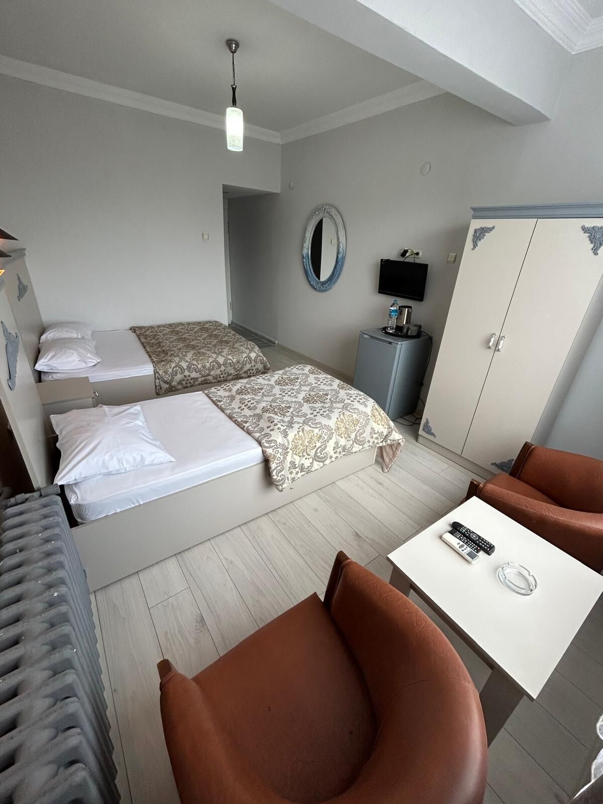 Habitación de hotel con dos camas, un escritorio, una silla, un armario, un espejo y un televisor.