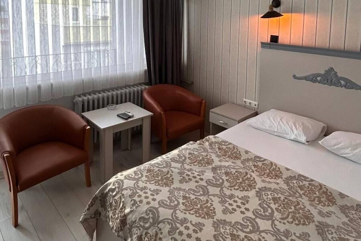 A hotel room with a bed, two armchairs, a small table, a lamp, and a window with curtains.