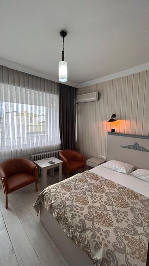 Ein Hotelzimmer mit einem Bett, zwei Sesseln, einem kleinen Tisch, einer Lampe und einem Fenster mit Vorhängen.