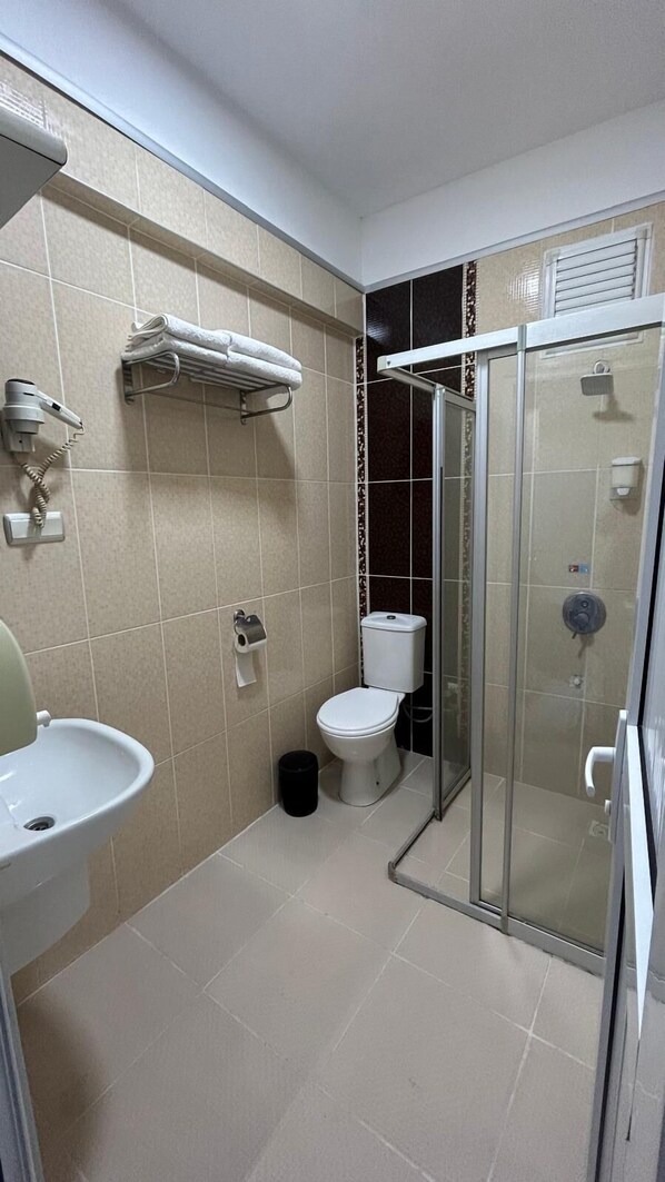 A bathroom with a toilet, sink, towel rack, and a glass shower enclosure. - Blue Dolphin Otel (Atakum)