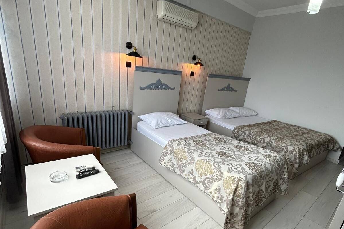 A hotel room with two beds, a small table, a brown leather chair, and a radiator.