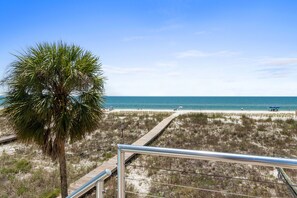 A beach with a palm tree, a wooden boardwalk, and a clear blue sky.