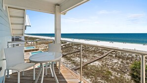 A balcony with a table and chairs, overlooking a beach with a clear view of the ocean and sandy dunes. - Clementine: 7 Bedrooms, Beachfront in Mexico Beach, Private Pool, Game Room (Mexico Beach)