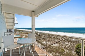 A balcony with a table and chairs, overlooking a beach with a clear sky.