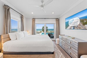 A hotel room with a bed, a TV, a view of the ocean, and a balcony.
