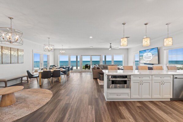 A spacious living area with a large island, dining table, and seating, overlooking a scenic ocean view.