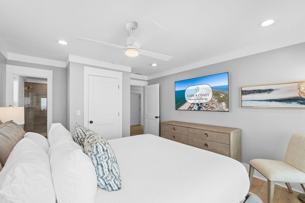 A bedroom with a bed, a ceiling fan, a dresser, a chair, and a wall-mounted TV. - Daiquiri: Beachfront in Mexico Beach, Private Pool, Pet Friendly (Mexico Beach)