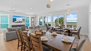 A spacious dining area with a view of the ocean, a large gray sofa, and a dining table set with plates and glasses. - Daiquiri: Beachfront in Mexico Beach, Private Pool, Pet Friendly (Mexico Beach)