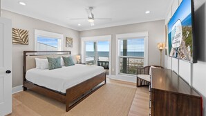 A bedroom with a large bed, a ceiling fan, and a view of the ocean through the windows. - Daiquiri: Beachfront in Mexico Beach, Private Pool, Pet Friendly (Mexico Beach)