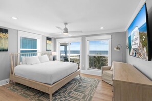 Una camera da letto con un letto, una scrivania, una sedia, una ventola a soffitto e un'ampia finestra vista mare.