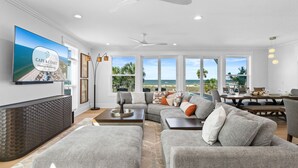 A spacious living room with a large TV, ceiling fans, a dining area, and a view of the ocean. - Daiquiri: Beachfront in Mexico Beach, Private Pool, Pet Friendly (Mexico Beach)