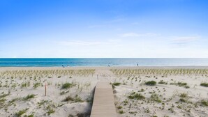 Een zandstrand met een houten loofpad naar het water, en enkele mensen in de verte.