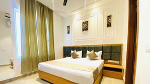 A hotel room with a large bed, a wooden headboard, and a bedside table. - Hotel MJ MARRIOTS (Amritsar)