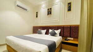 A neatly made bed with a wooden headboard, a bedside table with a phone, and an air conditioning unit on the wall. - Hotel MJ MARRIOTS (Amritsar)