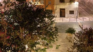 Nachtsicht auf eine Stadt mit beleuchteten Gebäuden, eine Kopfsteinpflasterstraße und einen Hügel im Hintergrund.