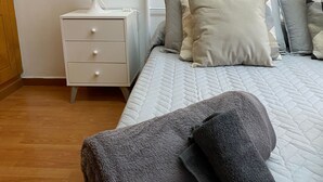 Ein ordentlich bezogenes Bett mit einer gesteppten Matratze und mehreren Kissen, ein weißer Nachttisch mit einer Lampe und ein Holzboden.