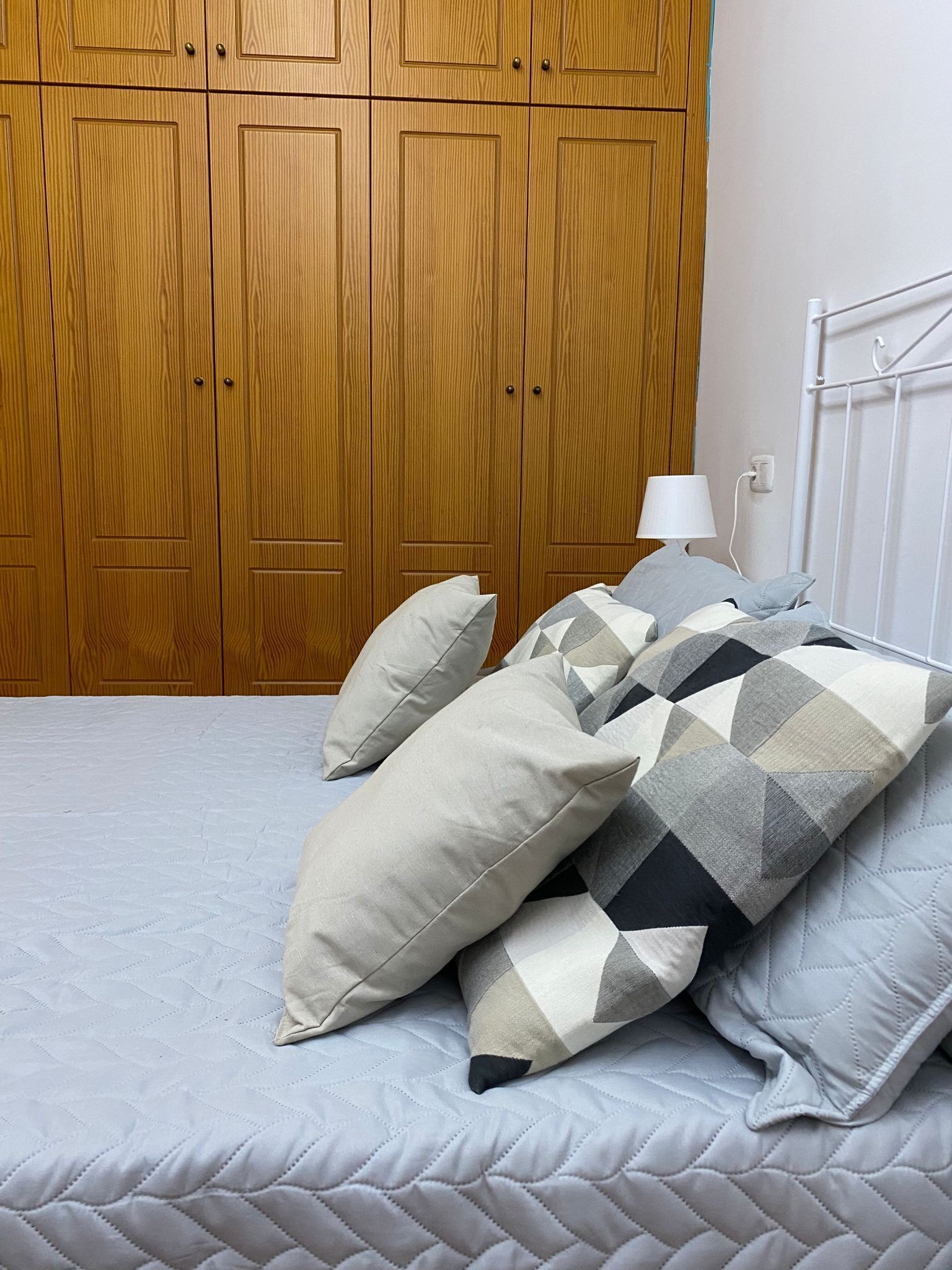 Un dormitorio con cama, almohadas, una lámpara de noche y un armario de madera.