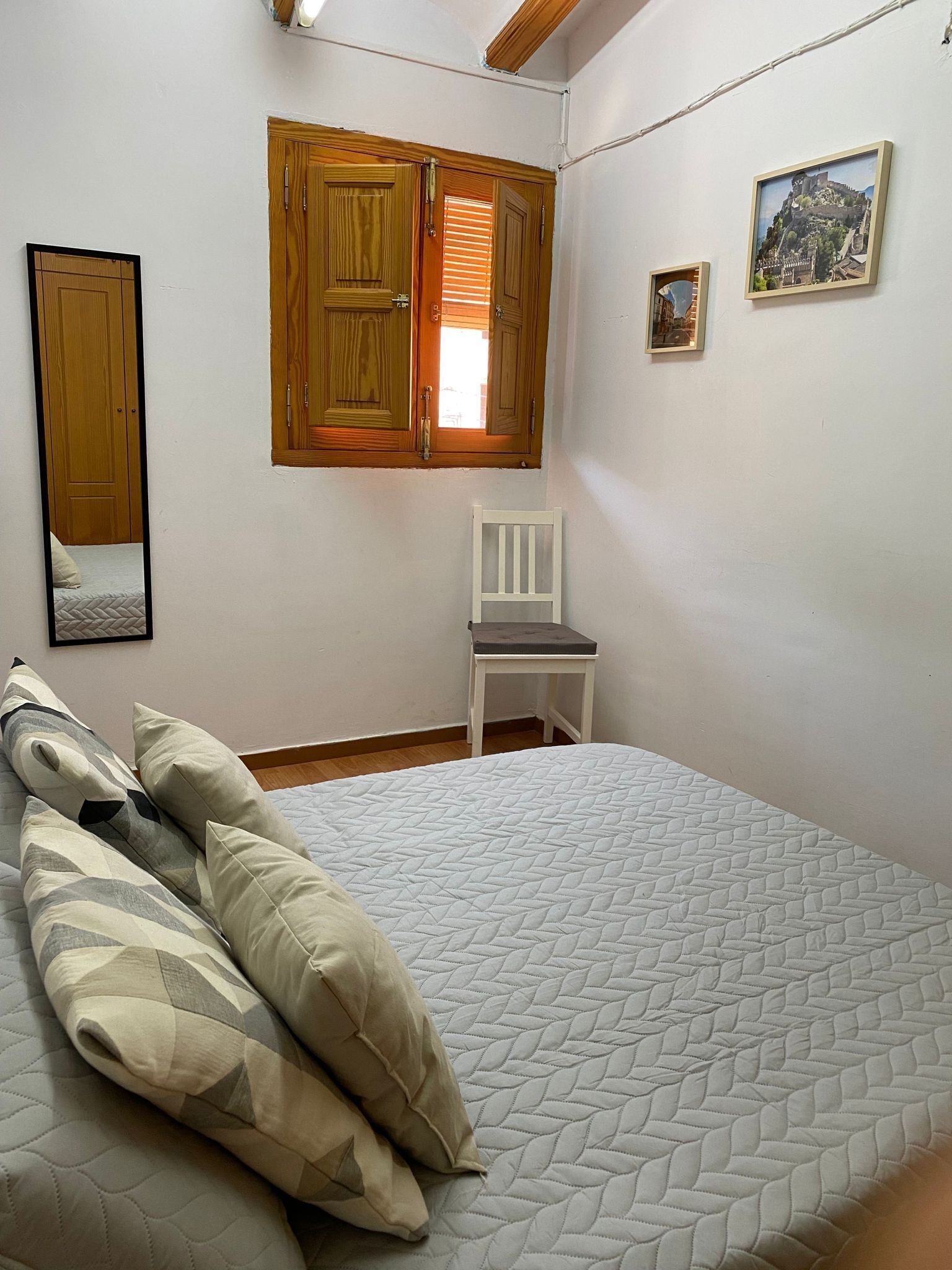 Ein Schlafzimmer mit einem Bett, einem Sessel, einem Fenster mit Holzjalousien und einem gerahmten Bild an der Wand.