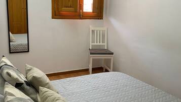 A bedroom with a bed, a chair, a window with wooden shutters, and a framed picture on the wall.