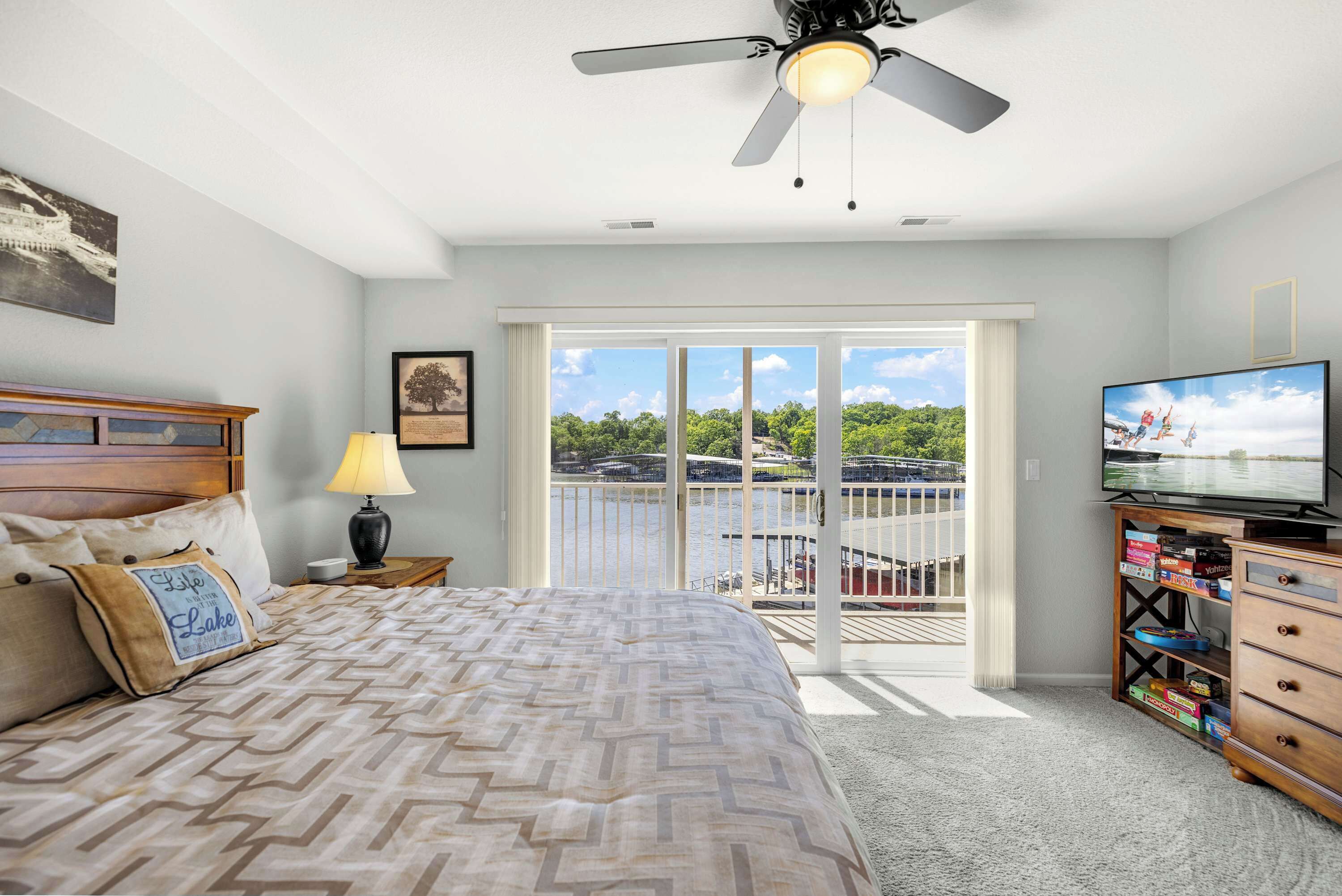 A bedroom with a bed, a television, a dresser, a lamp, and a balcony with a view of the water.