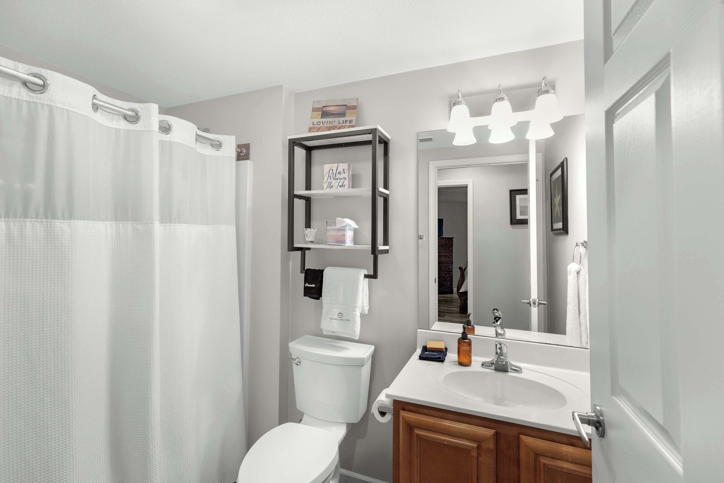 A bathroom with a toilet, sink, and shower curtain. There is a shelf with toiletries and a mirror above the sink.