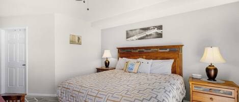 A bedroom with a bed, a nightstand, a wooden dresser, a ceiling fan, and a door.