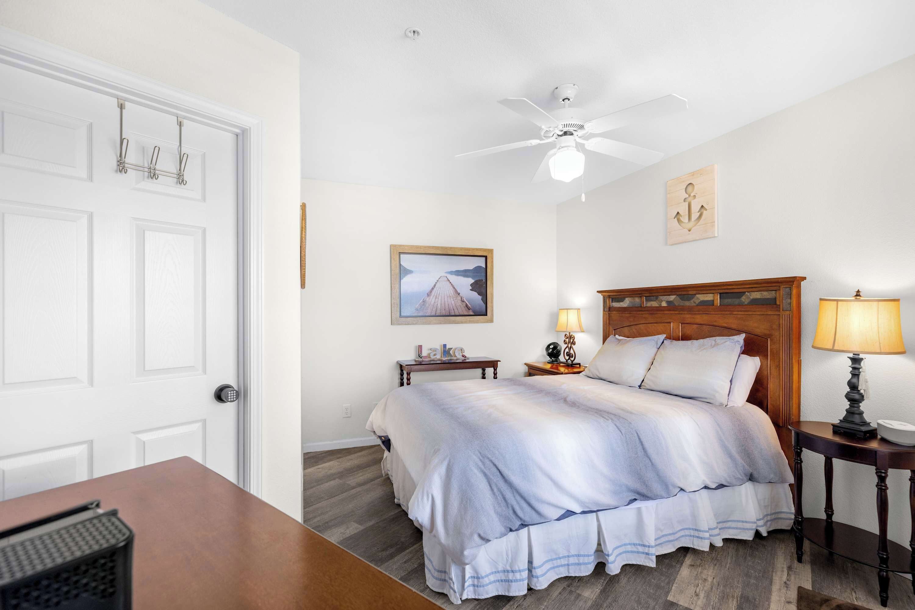 Une chambre à coucher bien rangée, avec un lit, des tables de chevet, un ventilateur de plafond et un tableau encadré au mur.